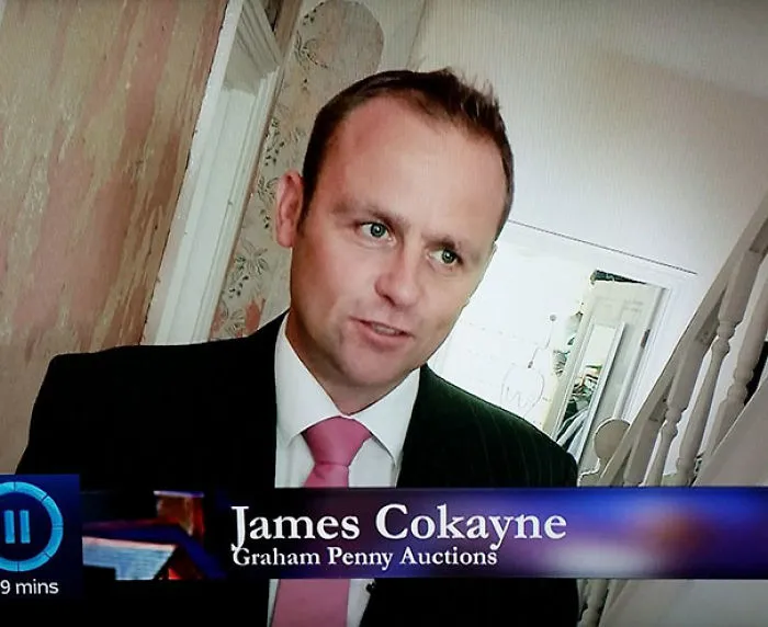 Person in a suit and pink tie with a humorous name tag displayed on screen.