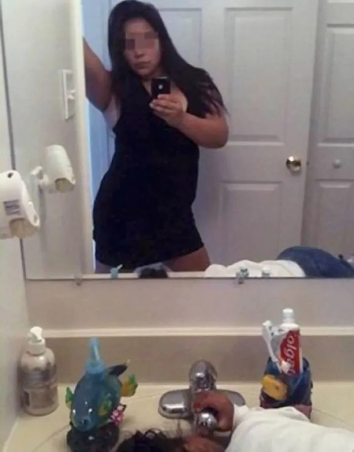 Woman taking mirror selfie while her kid drinks water from the tap