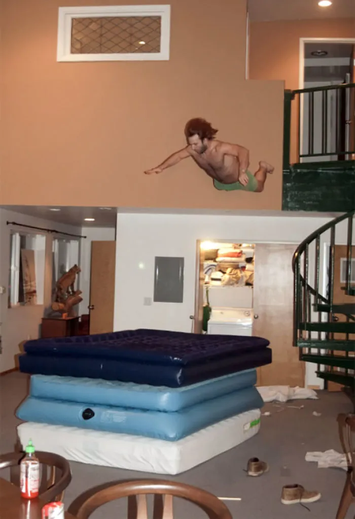 Man diving onto stacked air mattresses in a living room, illustrating why women live longer than men.