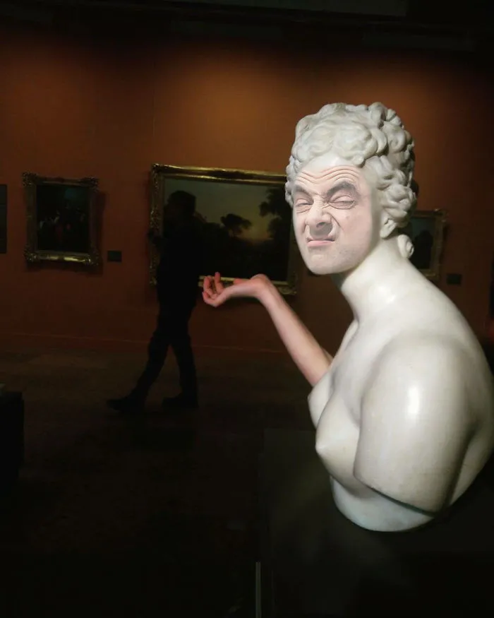 Marble statue in a museum with Mr. Bean's photoshopped face making a silly expression in an art gallery setting.