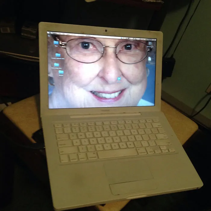 Older person struggling with technology, displaying a large face on a laptop screen.