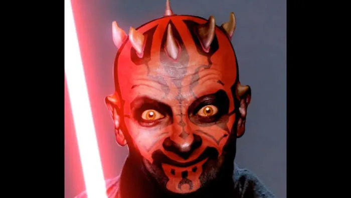 Man with devil-like makeup and horns holding a red lightsaber in a funny Mr. Bean Photoshopped image.