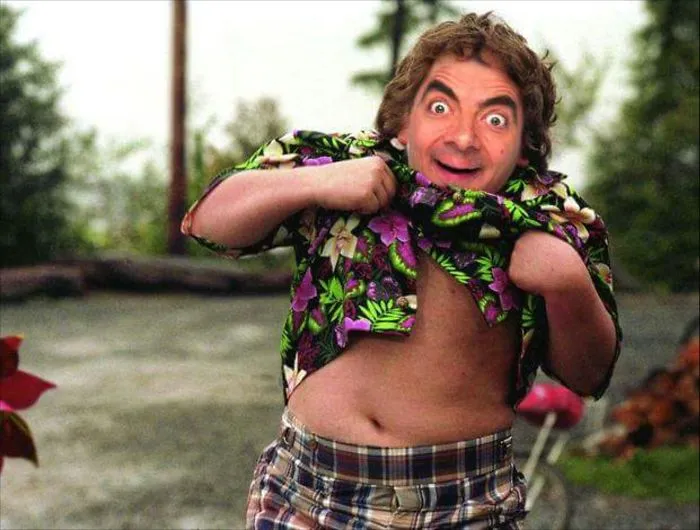 Photoshopped image of Mr. Bean lifting his Hawaiian shirt outdoors, showcasing a humorous and playful scene.