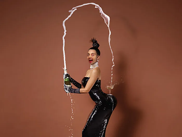 Person in glamorous black dress with champagne spraying, featuring Mr. Bean photoshopped face in a humorous edit.