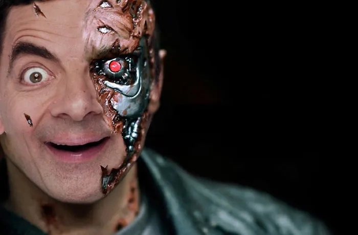 Mr. Bean photoshopped as a cyborg with a metallic robotic face and glowing red eye in a dark background.