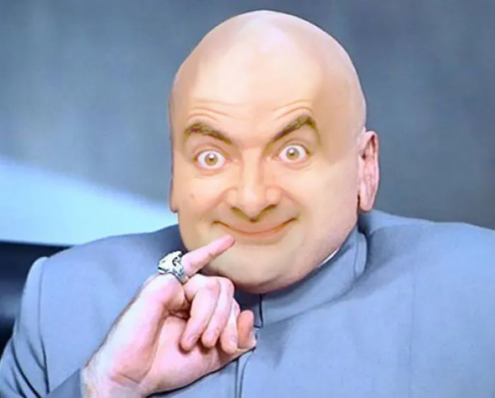Photoshopped image of Mr. Bean with a bald head, wearing a gray suit, making a mischievous gesture.