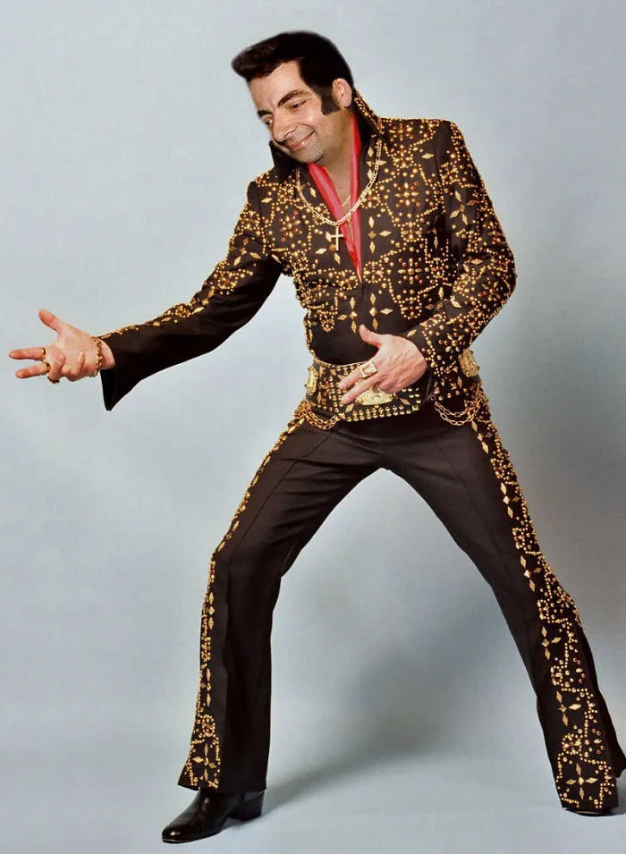 Mr. Bean photoshopped wearing a detailed black and gold Elvis-style jumpsuit posing against a gray background