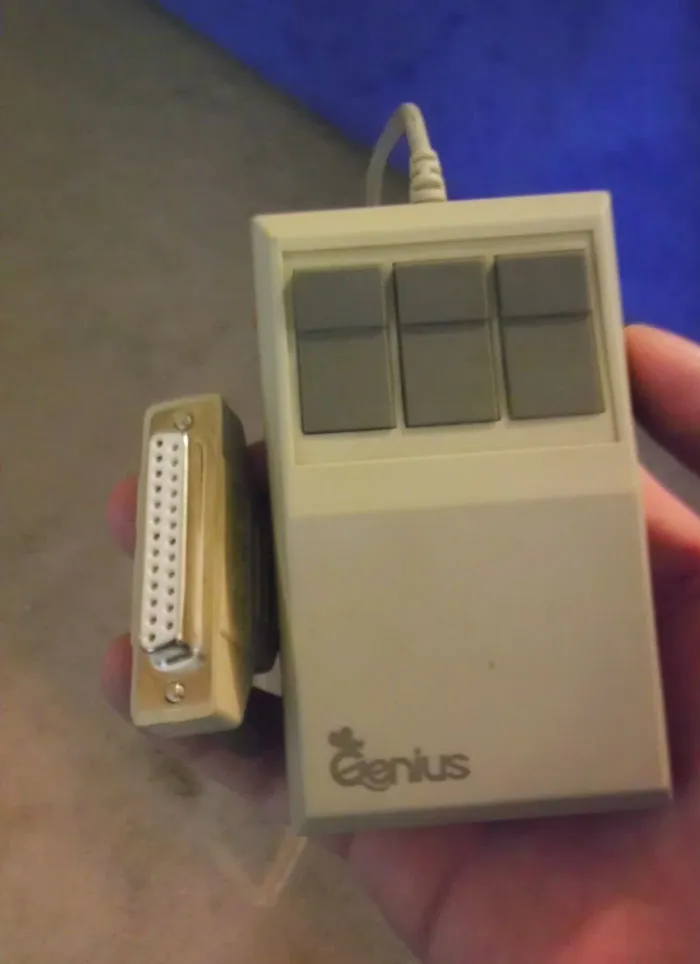 Older person's hand holding a vintage computer mouse with a large connector, illustrating technology challenges.