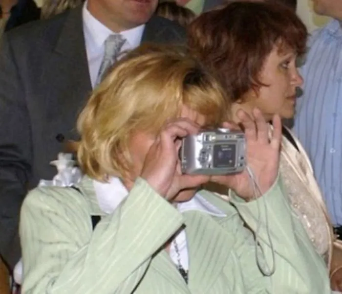 Older person humorously using digital camera incorrectly at an event.