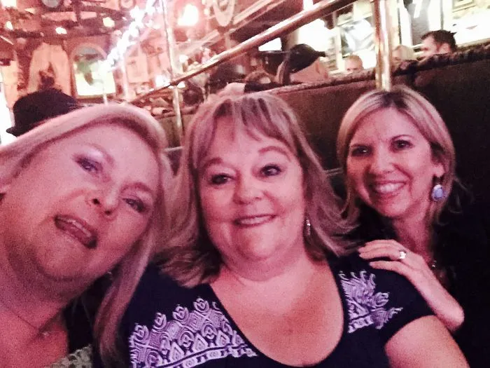 Three adult sisters smiling for selfie in casual indoor setting