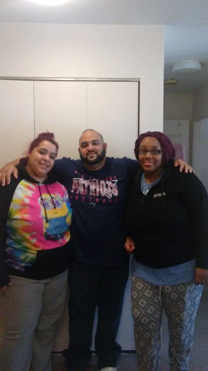 Three siblings standing indoors wearing casual clothes in recreated photo