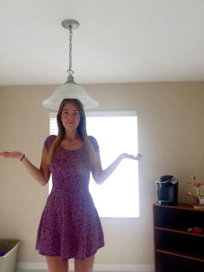 Woman standing under a low ceiling light fixture showing everyday struggles of tall people in a living room setting.