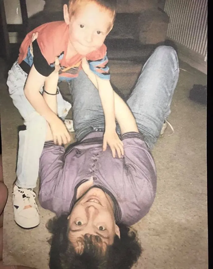 Young boy climbing on adult lying on floor in playful sibling moment