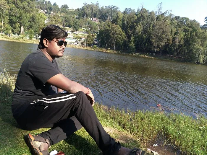 Man sitting by lake with sunglasses outdoors in casual wear