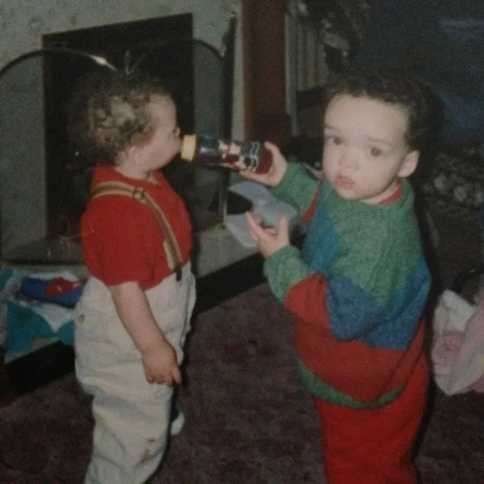 Two toddlers playing by fireplace with one drinking from a bottle