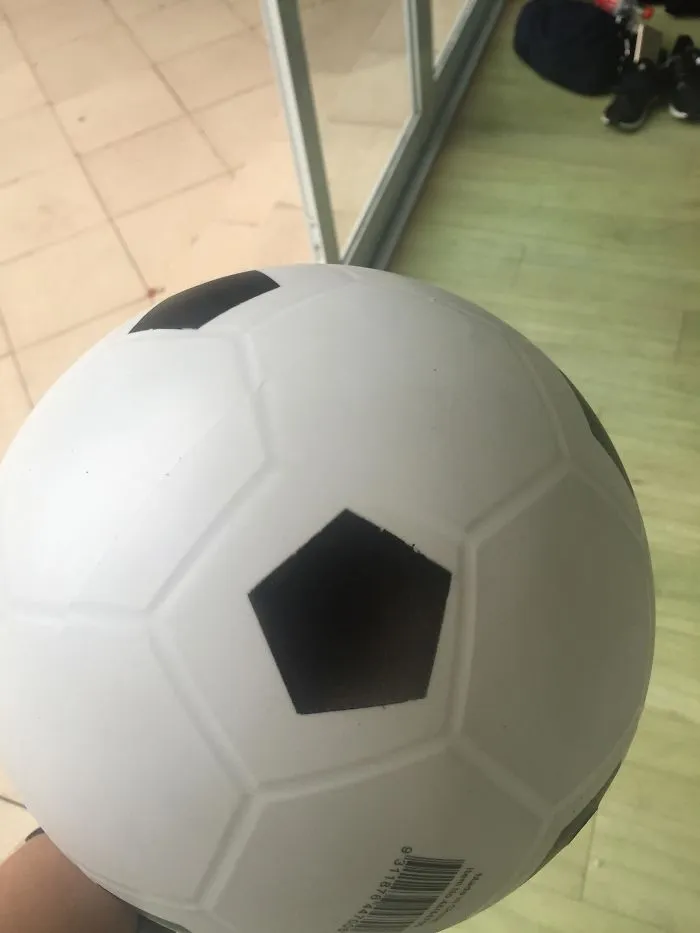 Soccer ball with mismatched pentagon design, indoors near a window, showcasing a funny design fail.
