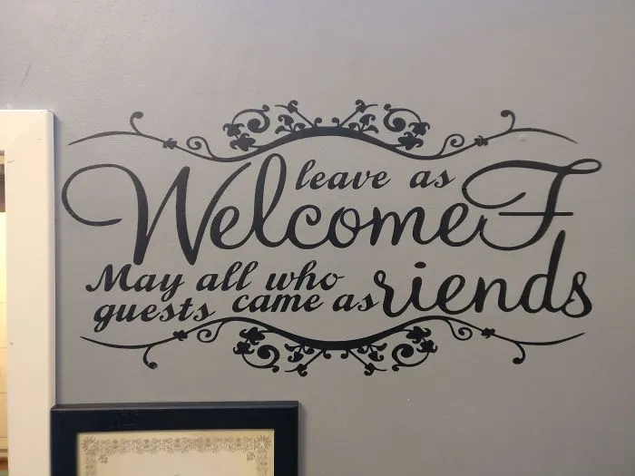Wall decal with design fail: "leave as WelcomF, guests came as riends." Decorative script on gray wall.