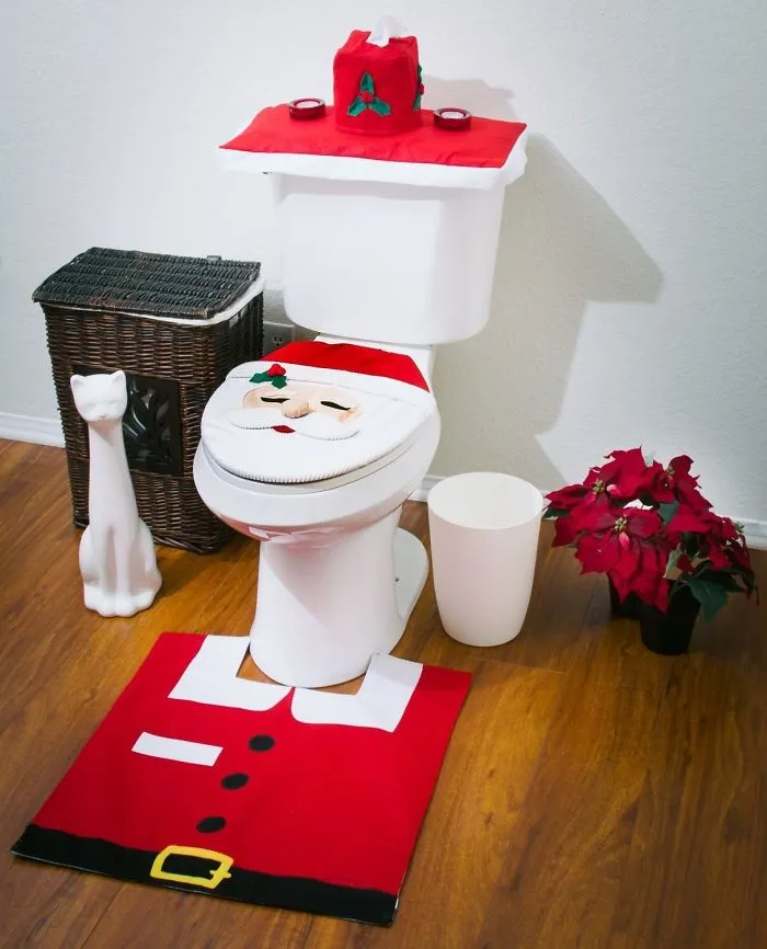 Santa-themed toilet decor with matching rug, alongside a wicker basket, cat statue, and poinsettia, showcasing a design fail.