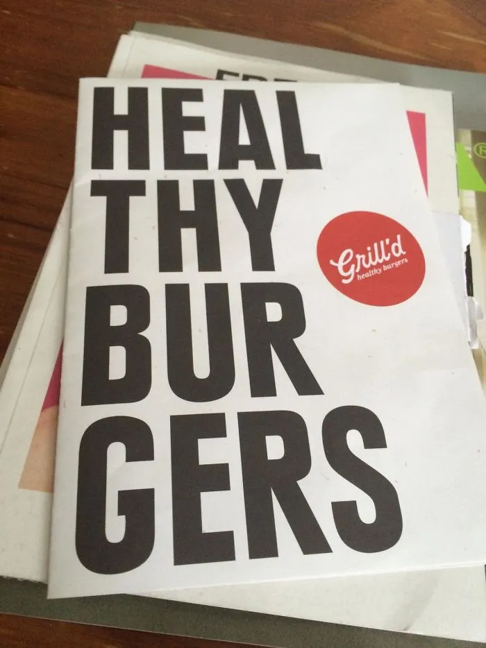 Brochure showing a humorous design fail with text reading "HEAL THY BUR GERS" for a burger restaurant.