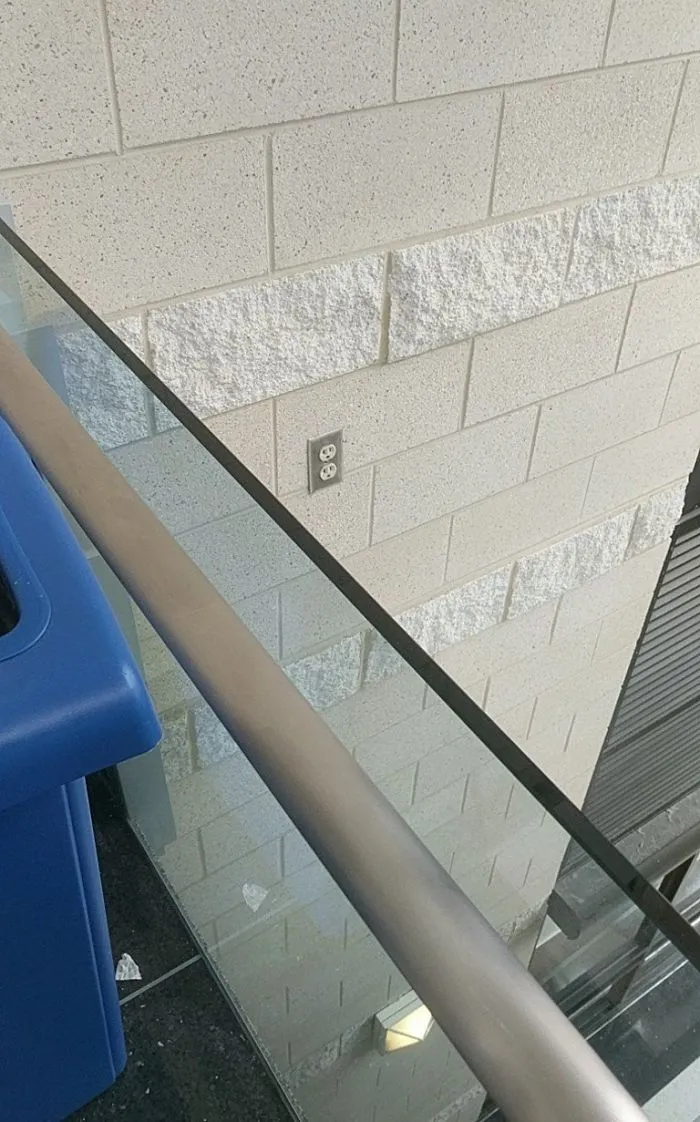 Electrical outlet positioned behind a glass railing, illustrating a design fail.