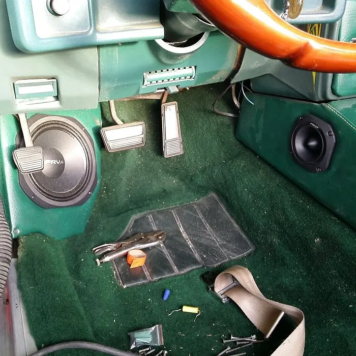 Car interior design fail with misplaced pedals and speakers on green carpet flooring.