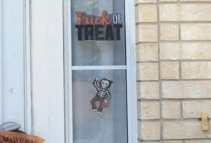 Halloween decor design fail with a skeleton and "Trick or Treat" sign on a glass door.