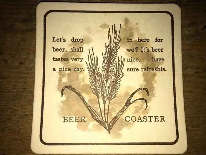 Humorous design fail on a beer coaster with garbled text and wheat illustration.