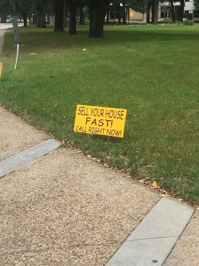 Yellow sign on grass reads, "Sell your house fast! Call right now!" showcasing a design fail on a city sidewalk.