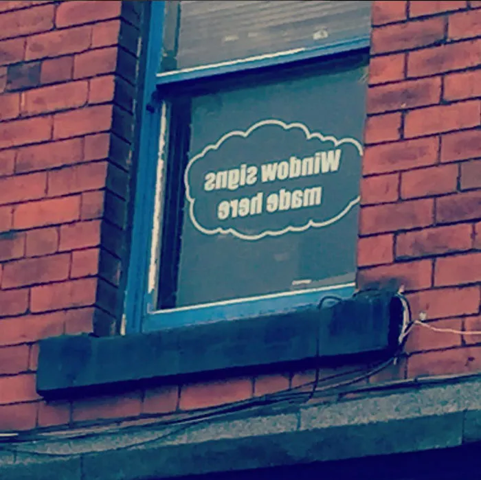 Reversed window sign on a brick building, reading "Window Signs Made Here," illustrating a humorous design fail.