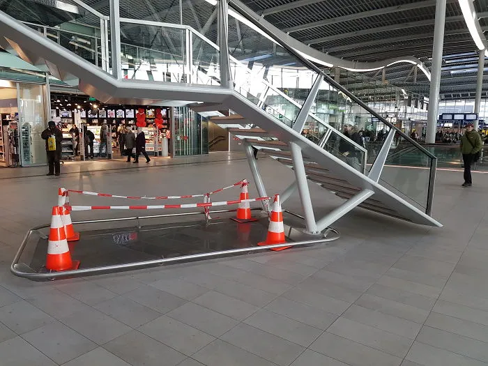 Staircase design fail with stairs leading to nowhere, surrounded by caution cones in a shopping center.