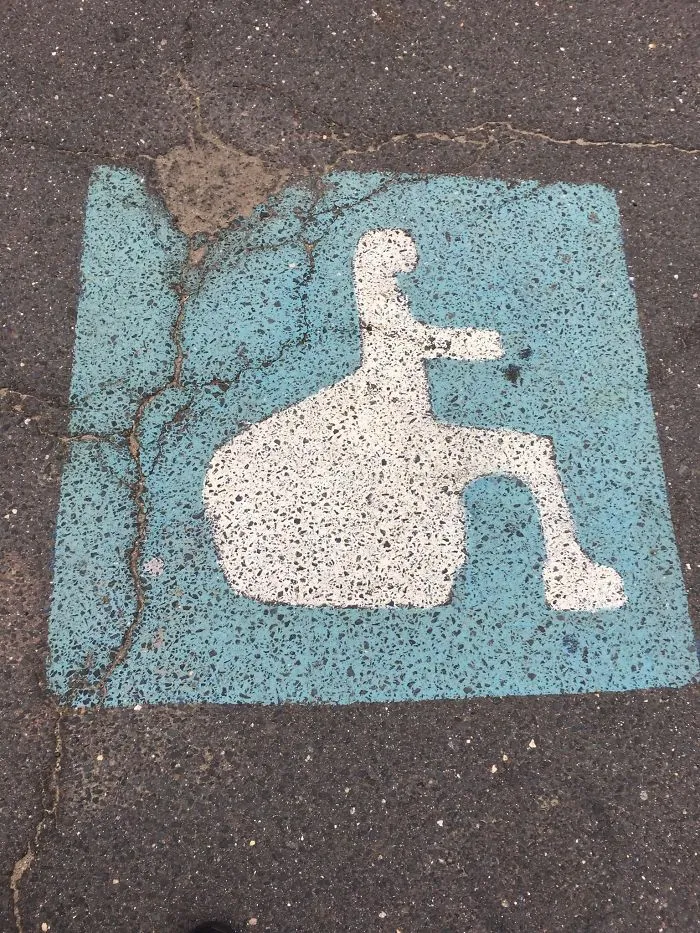 Incorrect handicapped parking sign design fails with unusual shape on pavement.