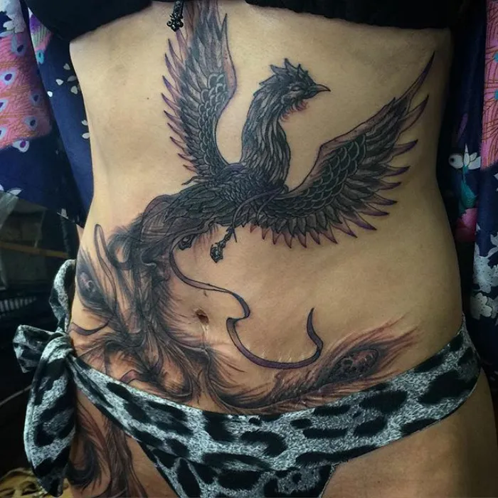 Phoenix tattoo beautifully transforming a scar on a person's abdomen, showing the art of scar cover-up.