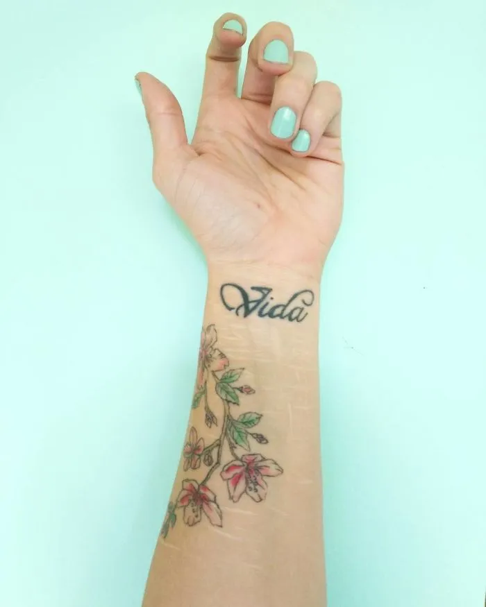 Floral tattoo on wrist beautifully transforming scars, featuring the word "Vida."