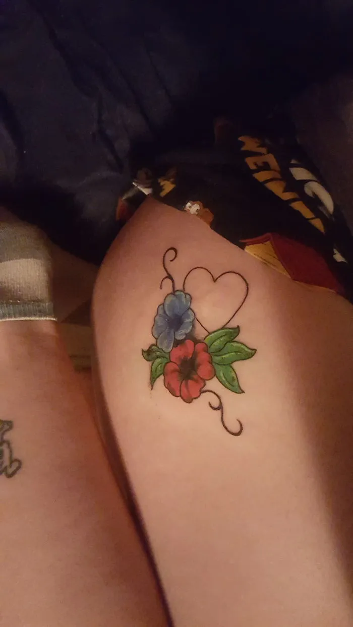 Floral tattoo covering a scar with vibrant red and blue flowers and a heart outline, turning scars into art.