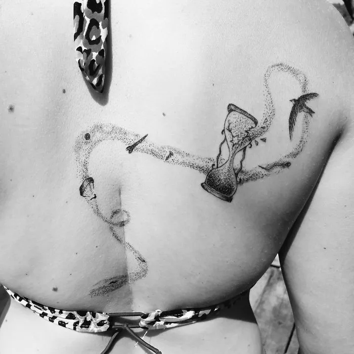 Tattoo art on a back, featuring an hourglass and bird, transforming a scar into a stunning design.