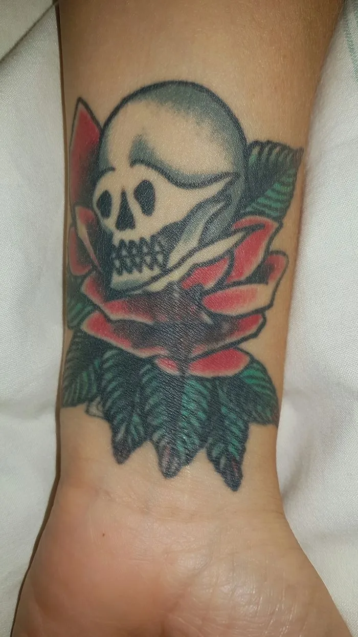 Tattoo of a skull and rose beautifully transforming a scar into art on a wrist.