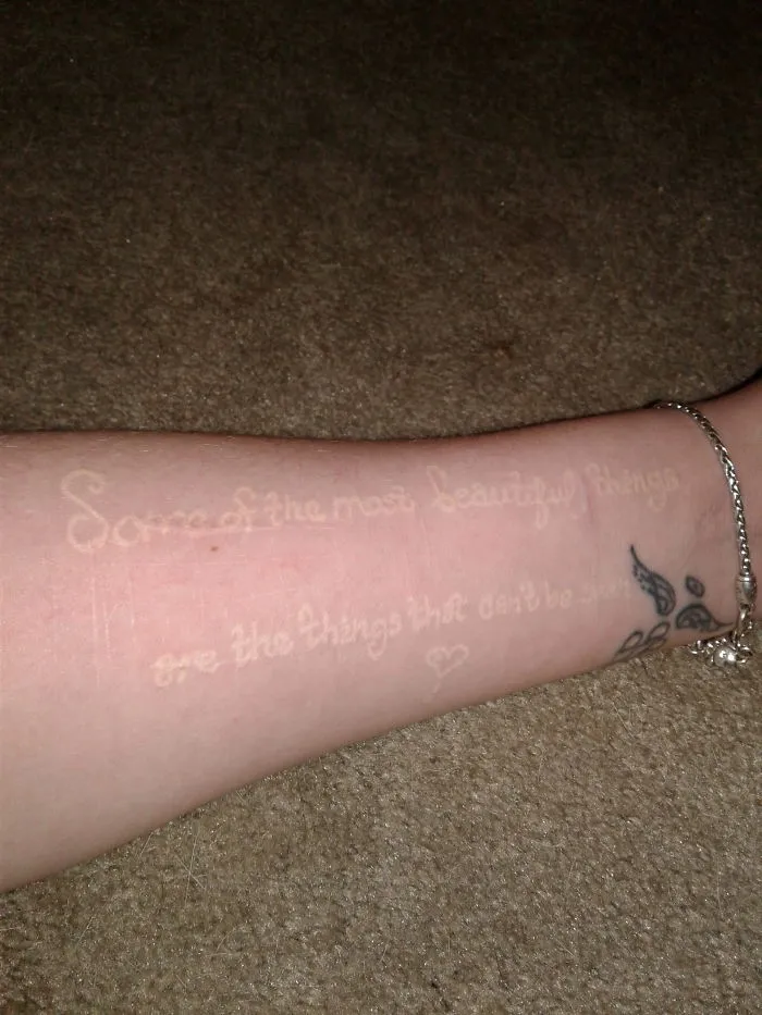 Tattoo art covers a scar on an arm with a quote, creating a meaningful design to transform the scar into art.