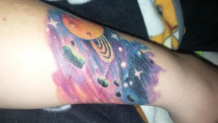 Colorful space-themed tattoo transforming a scar into art on an arm.