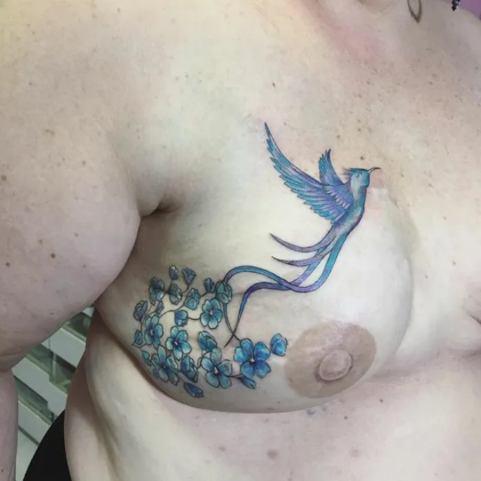 Tattoo of a blue bird and flowers creatively transforming a scar into art on a person's chest.