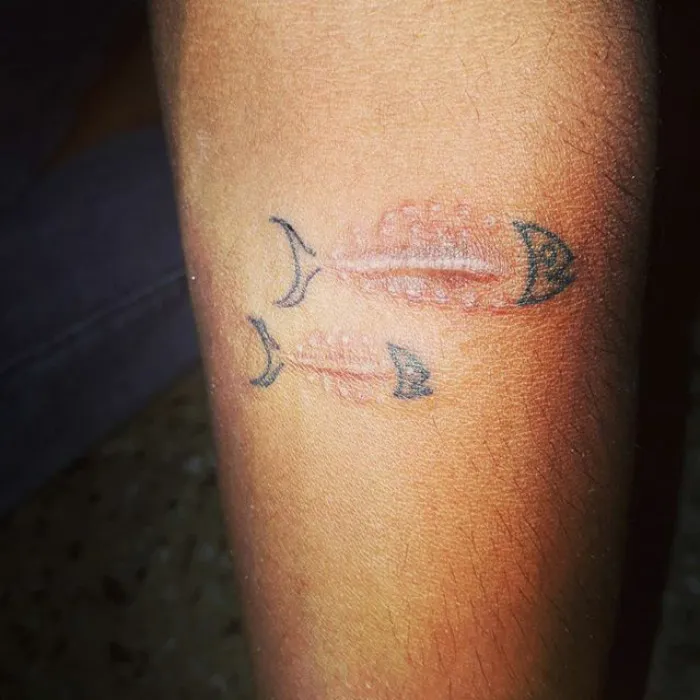 Tattoo of fish bones creatively incorporating a scar into the design on skin.