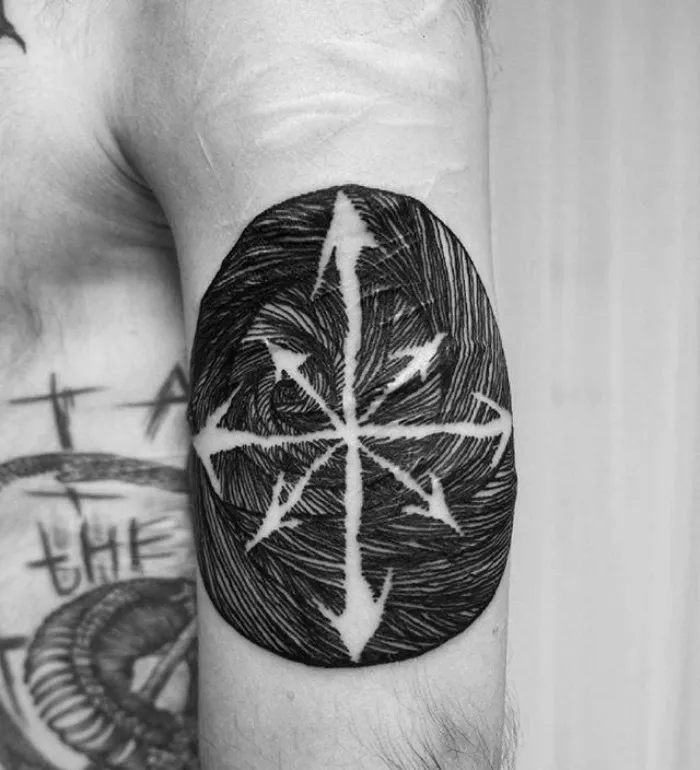 Tattoo art on arm blending with scar, featuring a compass design in black ink.