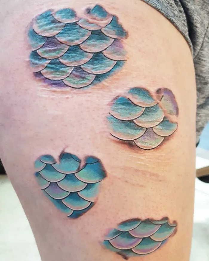 Tattoo art transforms scars into vibrant blue-green scales on skin.