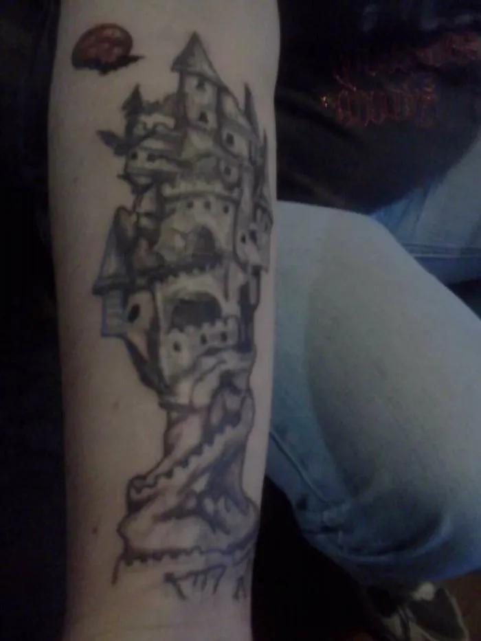 Tattoo of a castle creatively designed to transform a forearm scar into art.