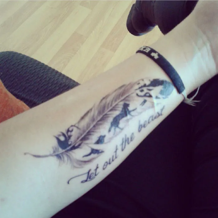 Tattoo featuring a feather and text "Let out the beast" on a forearm, transforming a scar into art.