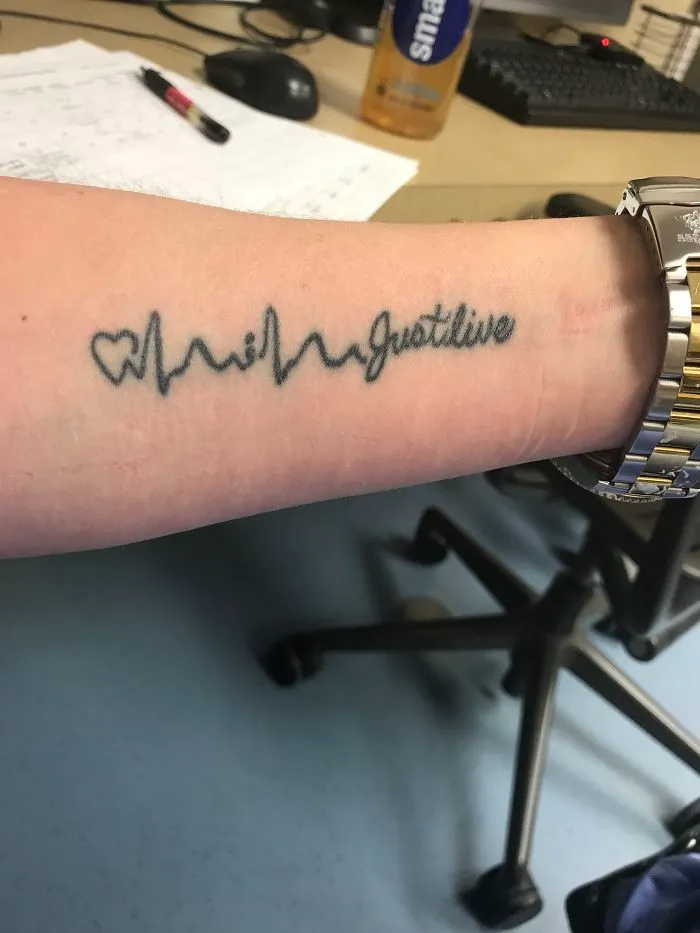 Tattoo covering a scar with a heartbeat line and "Just live" text on an arm.