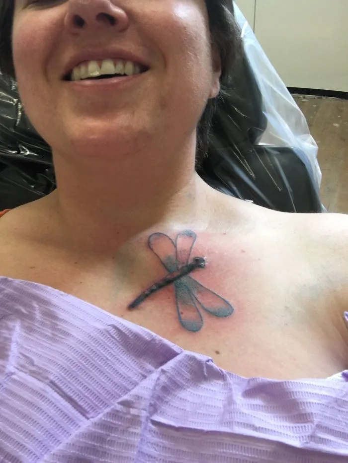 Woman with a dragonfly tattoo on her chest turning scars into art, wearing a purple gown, smiling.