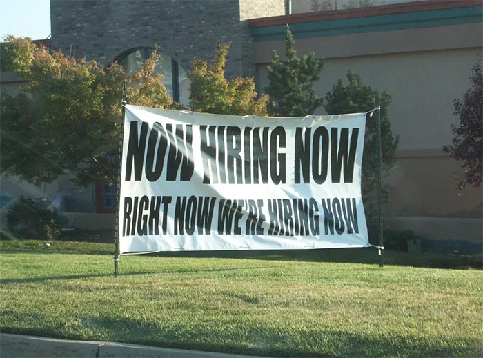 Banner displaying repetitive "Now Hiring" message, illustrating a design fail on a green lawn.