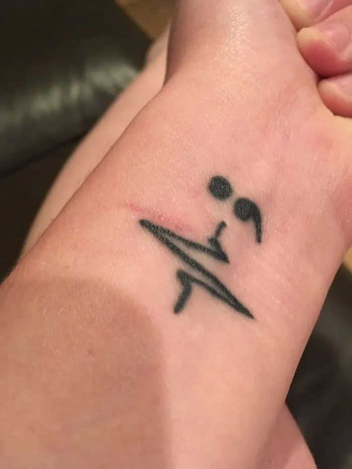 Tattoo turning a scar into art with a semicolon design on a person's wrist.