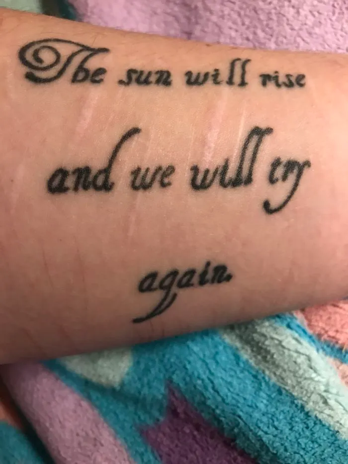 Tattoo with text "The sun will rise and we will try again" covering a scar, turning it into art.