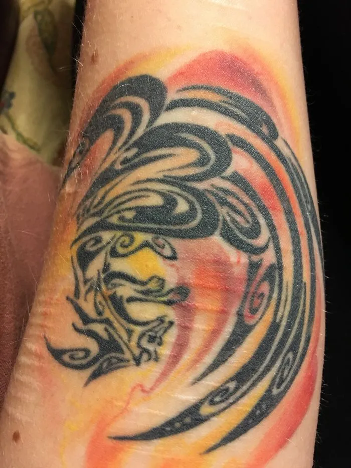 Tattoo design transforming a scar into art with swirling patterns in black, red, and yellow hues.